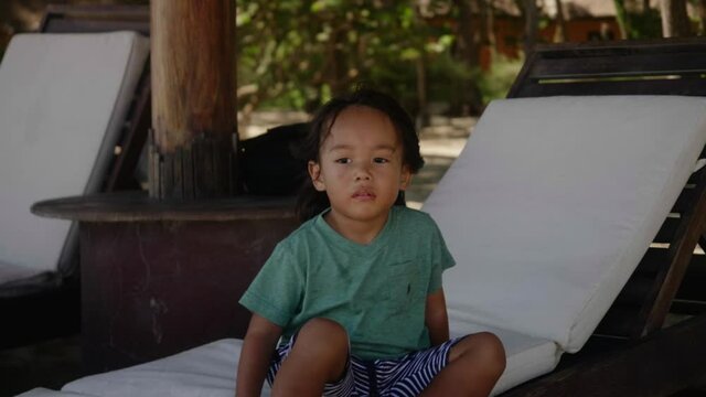 Wideshot of an Asian boy sitting on beach deck chair.