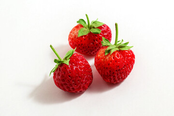 three ripe, red, fresh strawberries, close-up on a white background