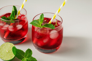 cold homemade strawberry lemonade with ice in glass glasses, mint leaves, lime slices and berries on a white table