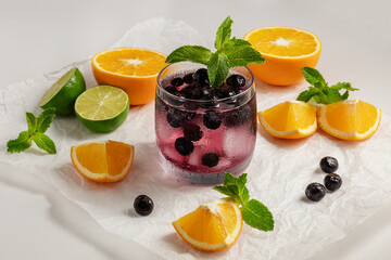 cold homemade blueberry lemonade, in a glass glass, pieces of citrus on a light background