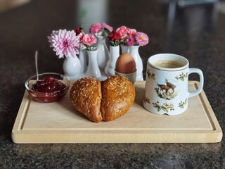breakfast on the Sunday morning with freshly backed pastries, cooked egg, cranberry jam and hot coffee on a wood board and a vase with spring flowers in the background