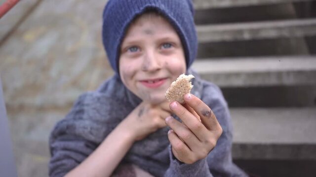 homeless boy sits on stairs in bandoned place holding bread in his hand migration homeless child with a dirty face and hands needs help Social problems custody Homeless people refugee escape from war