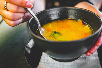 Woman hand eating chicken soup in black bowl sitting in cafe