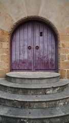 Fototapeta na wymiar A beautiful pink door with arches, on a red brick wall, imposing on round steps, in the Gijon, Spain