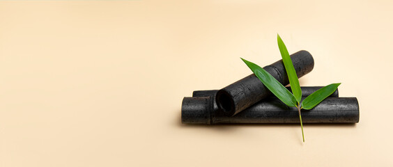 Bamboo activated charcoal sticks and green leaf on cream color  background.
