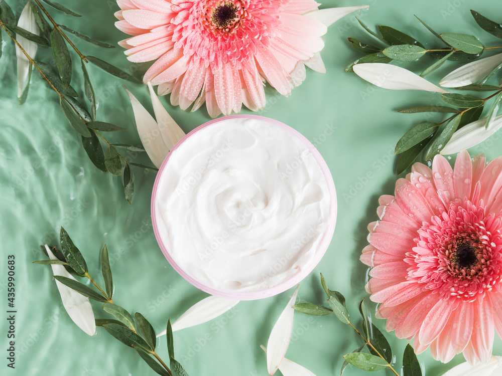 Wall mural Skin care flat lay with generic cream jar with pink gerbera in water on green background