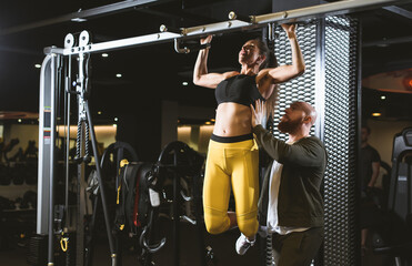 Muscular woman fitness model doing pull-ups. The coach looks after the correctness of the exercise. Fitness bikini competition preparation concept