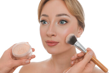 Professional makeup artist applying powder onto beautiful young woman's face with brush on white...