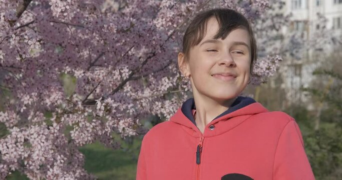 Girl with rhinitis. A view of a young girl with seasonal allergy rhinitis sneeze between blooming trees in the meadow.