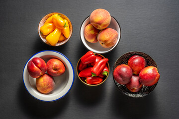 Top view of several assorted bowls of nectarines, peaches, and red and yellow bell peppers