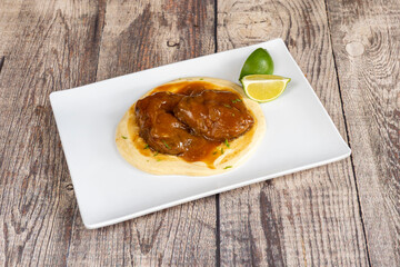 Rectangular white plate of braised cheeks on bed of mashed potatoes