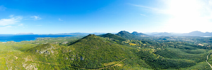 Fototapeta na wymiar View from above, stunning aerial view of a mountain range covered by a green vegetation with a beautiful coastline bathed by the mediterranean sea. Sardinia, Italy.