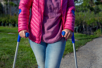 Frau in pinkfarbener Jacke und Blue Jeans mit Krücken draussen beim Spaziergang