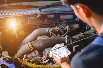 Asian mechanic working in an auto repair shop is checking the oil level for a customer who is servicing a car or changing the engine oil in a garage.