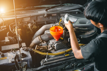 Asian auto mechanic works in auto repair shops. Pour the engine oil to change the engine oil in the...