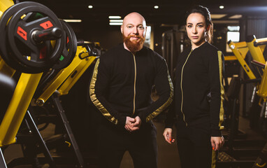 Fototapeta na wymiar A group of people: an athletic woman and a muscular man. Team of trainers in the same clothes posing for the camera against the background of the gym