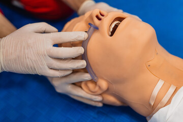 CPR training of paramedics in red uniforms holding a tube in the dummy's nose. First aid, close-up