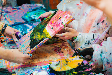 Little children's hands pouring acrylic paint onto a canvas. Abstract painting technique fluid art