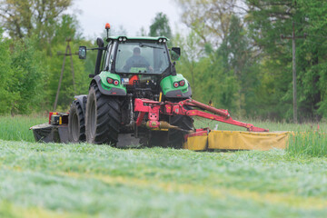 Koszenie trawy przy użyciu ciągniętej przez traktor kosiarki rotacyjnej. - obrazy, fototapety, plakaty