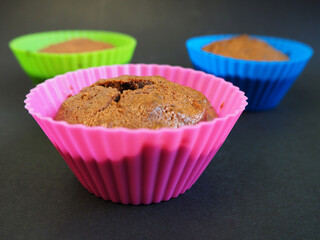 Close-up on black background homemade gluten-free chocolate muffin with apples in pink, light green and blue silicone mold. side view . gluten free baked goods
