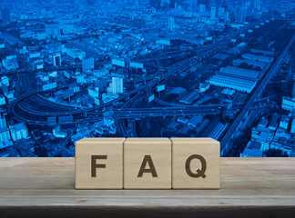 FAQ letter on block cubes on wooden table over modern city tower, street, expressway and...