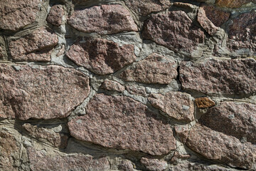 Old stone masonry made of granite. Red granite stones of different shapes and sizes. Background texture.