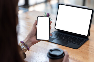 Close-up of a woman hand holding a smartphone and tablet a blank white screen is placed at the office desk. Mock up.