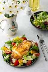 Delicious hearty lunch, chicken breast baked with spices and a mix of salad with tomatoes, radishes and cauliflower, a plate of salad and daffodils in a vase