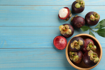 Fresh ripe mangosteen fruits on light blue wooden table, flat lay. Space for text