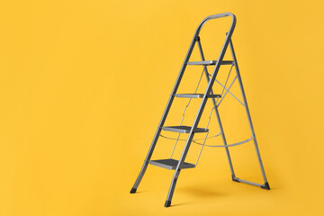 Modern metal stepladder on yellow background. Space for text