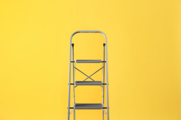 Modern metal stepladder on yellow background. Construction tool