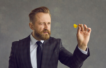 Studio headshot portrait of businessman in formal wear squinting eye aiming with dart arrow holding focus on invisible target. Goal and purpose, challenge and mission, strategy and ambition concept