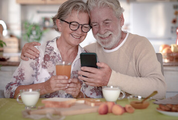 Smiling senior couple looking cellphone during breakfast at home