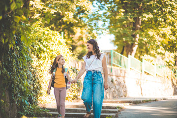 Little girl walking to school with her mother in nature.
