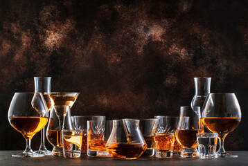 Hard strong alcoholic drinks, spirits and distillates in glasses in assortment: vodka, cognac, scotch, whiskey etc. Brown bar counter background