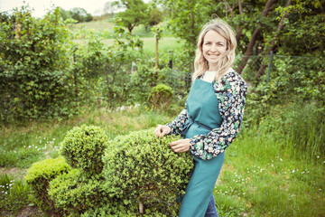 young pretty blonde gardener with green apron and blue rubber boots and shirt with floral motifs...