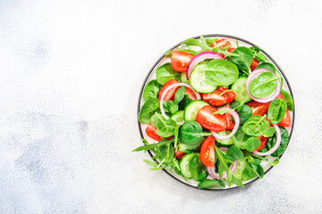Summer vegan salad with spinach, tomatoes, arugula, cucumber and red onion. Fresh and Healthy food. Gray stone table. Top view