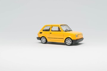 Maluch samochód zabawka koloru żółtego stojący bokiem na białym tle - obrazy, fototapety, plakaty