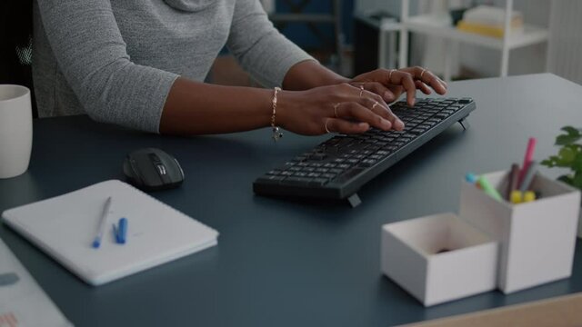 Close-up of student with black skin hands typing on keyboard searching information on internet working at business article sitting at desk table. Young woman browsing news message on computer