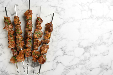 Metal skewers with delicious meat on white marble table, flat lay. Space for text