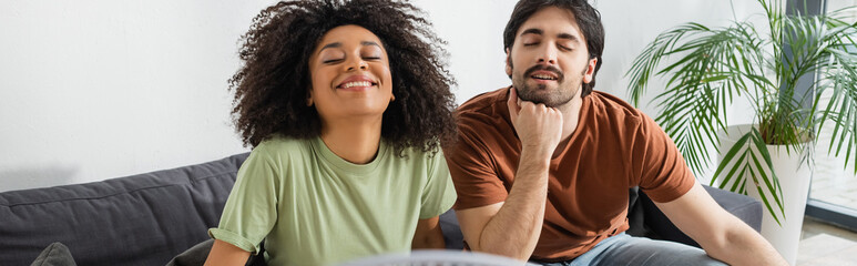 happy interracial couple sitting on couch in living room, banner