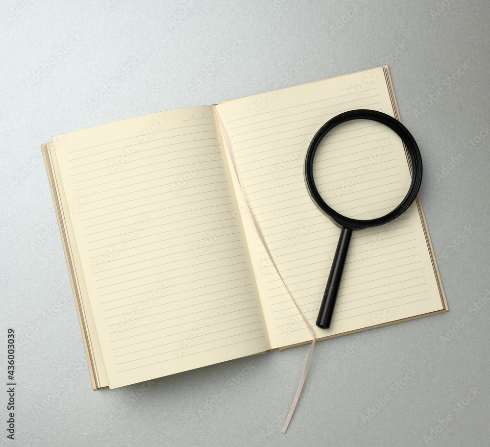 Poster paper notebook with blank white sheets and a black magnifier on a gray background