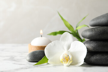 Obraz na płótnie Canvas Spa stones, bamboo sprout, burning candle and beautiful orchid flower on white marble table, space for text