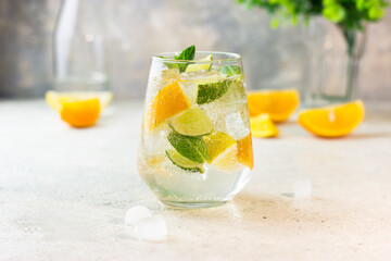 Lemonade with lemon, lime, tangerine, mint and ice cubes in glass on gray stone background. Cold summer refreshing drink or beverage.