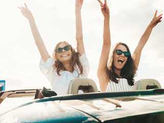 Portrait of two young beautiful and smiling hipster female in convertible car. Sexy carefree women...