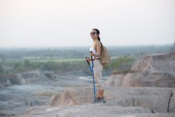 Fit female hiker with backpack and poles standing on rocky mountain ridge looking out valleys and...