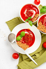 Tomato soup with crispbread and basil in white bowls on a gray background top view. Tasty summer food. Copy space for text.