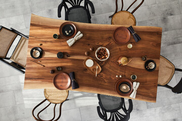 Stylish interior design of dining room with wooden walnut table, retro chairs, tableware, plates, tablecloth, teapot, food, decoration and elegant accessories. Cement floor. Template. Top view.