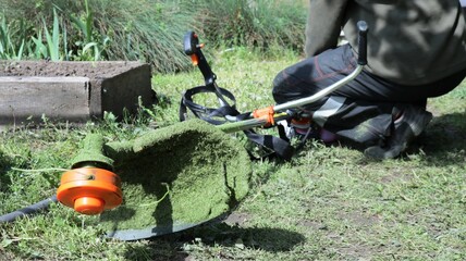 cutting part of a lawn mower lying on the ground in a garden with fresh grass adhered and a person...