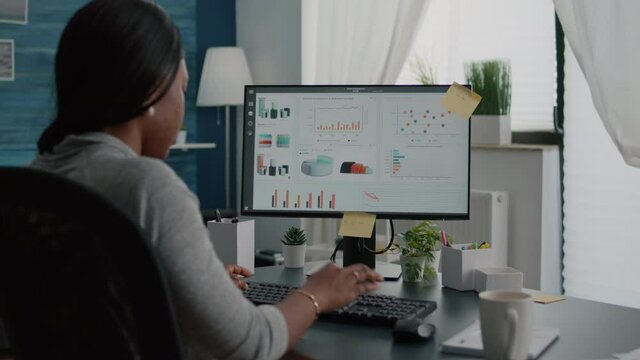 Closeup of black student browsing financial infographics analyzing statistics on laptop computer working at high school webinar. Woman sitting at desk table in living room typing commerce chart graph
